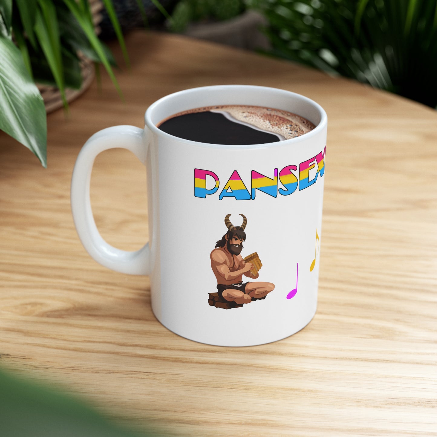 A white ceramic mug with the god Pan on it. Above, the word "pansexual" is partially seen, coloured in the pan pride flag colours. To the right of him, you can see a single purple and yellow note, partially obscured. The cup has coffee in it, and is sitting on a wooden table.