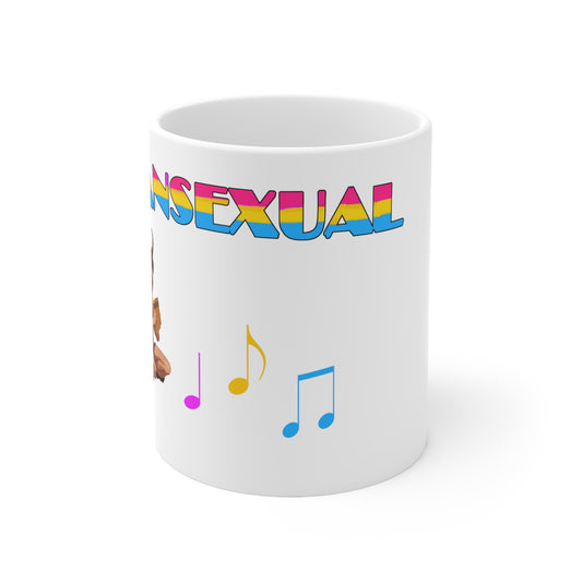 A white ceramic mug with the word "pansexual" written on it, partially obscured, in the pan pride colours. To the bottom left, you can vaguely see pan. Near the middle at the bottom are 3 music notes in the pan pride colours.