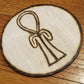 A wooden circle with a stylized ankh burned into the center of it.