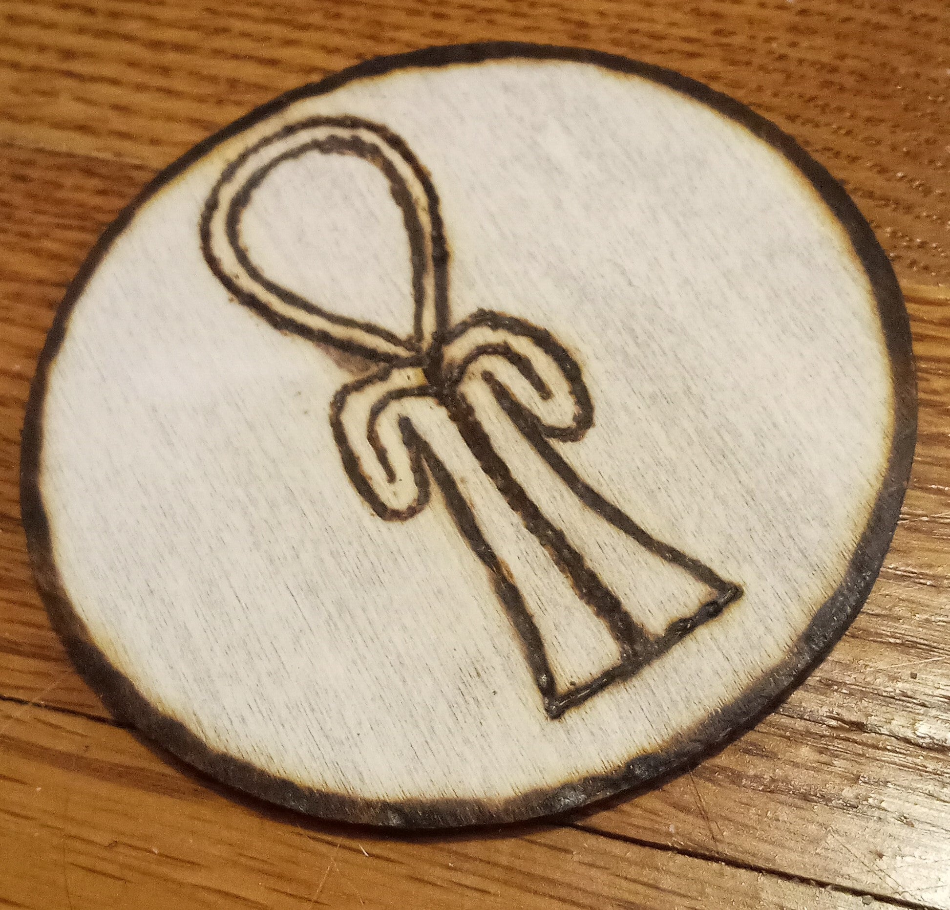 A wooden circle with a stylized ankh burned into the center of it.