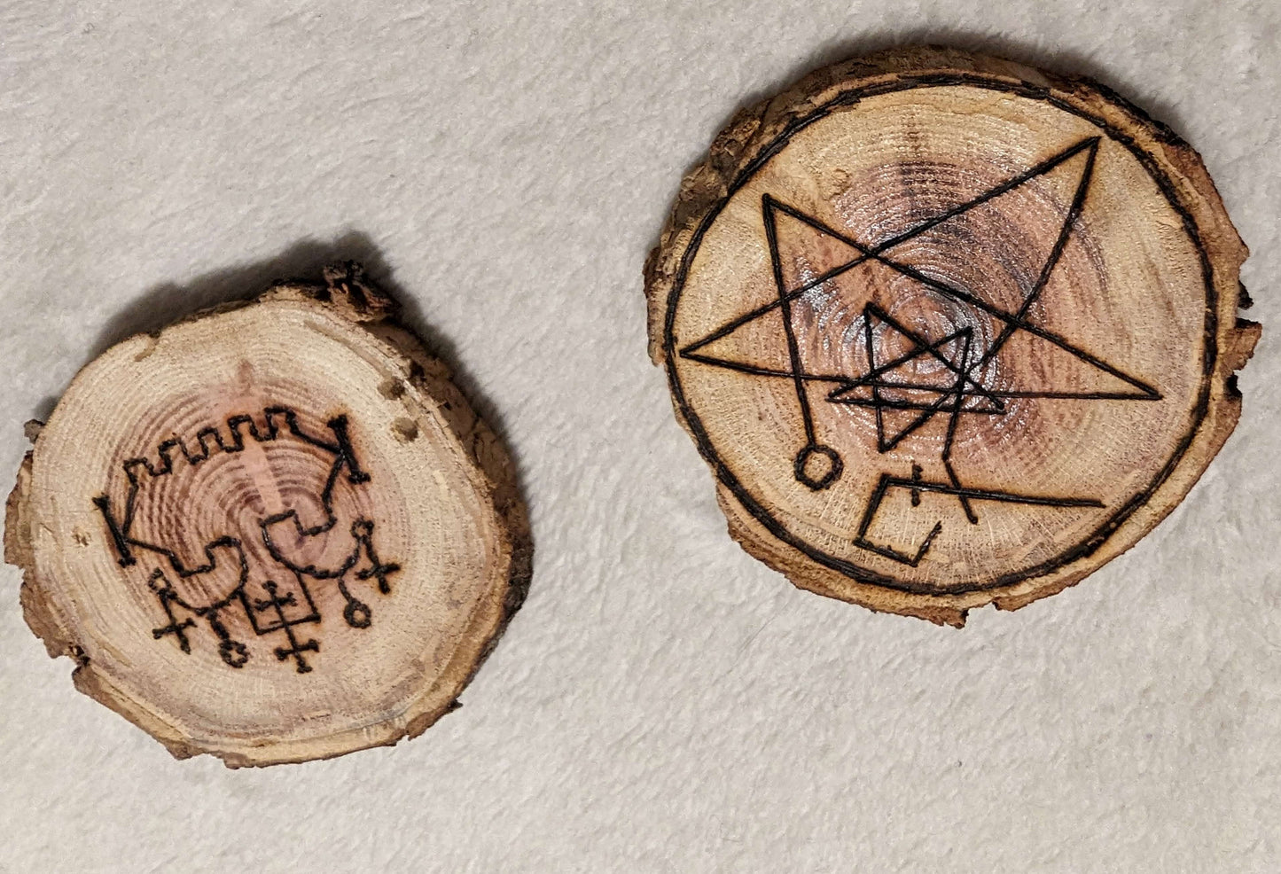 Two wooden sigils. One is the sigil for Belial. The other is So a sigil of the covenant of the elder gods, a symbol of GANZAR, and the sigil of the watcher, combined into a talisman.