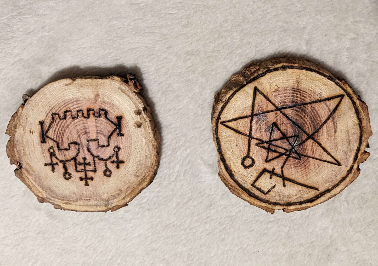 Two wooden sigils. One is the sigil for Belial. The other is So a sigil of the covenant of the elder gods, a symbol of GANZAR, and the sigil of the watcher, combined into a talisman.