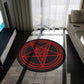 A large baphomet rug sitting in front of a couch in a living room. The rug itself is black with red rings. The inner ring has lines spaced evenly. The center forms a pentacle with a goats head, it's horns at the top points, and its beard flowing down to the bottom. It has a pentagram on its forehead.