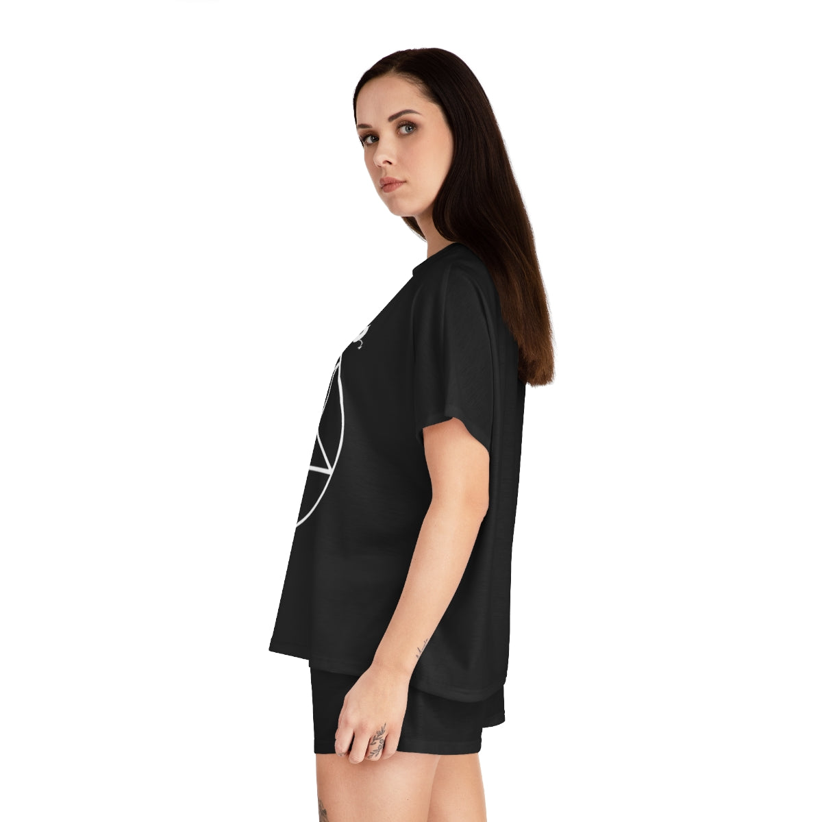 A side view of a woman with long black hair wear a black pajama shirt and black pajama shorts. You can see part of a pentacle and part of a chibi cat demon on the shirt.