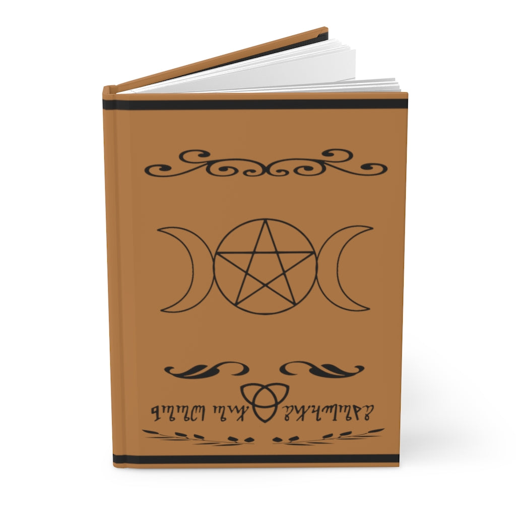 A brown book of shadows. The middle showcases a triple moon pentacle. The bottom shows a celtic knot with the words "Book of shadows" written in theban script. The book is opened slightly.