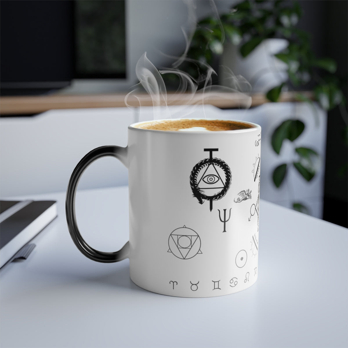 A white mug with a black handle sitting on a table. There's coffee with steam coming out of the mug. On the mug is an assortment of alchemical symbols. Towards the top is an Ouroboros with an all seeing eye staked through the center. Just below is a trident. Below, and to the left, is a symbol for the philosopher's stone. To the bottom right of that is the symbol for sol. Below all of it are an assortment of the zodiac signs.