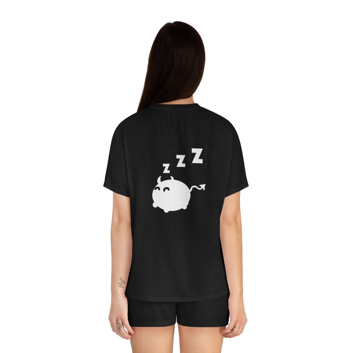 The back view of a woman bearing a black pajama shirt and black pajama shorts. he shirt has a sleeping cat demon with 3 z's above their head in the middle.